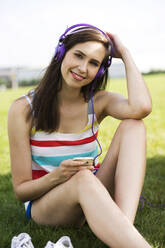 Lächelnde Frau hört Musik über Kopfhörer im Park - MIKF00084