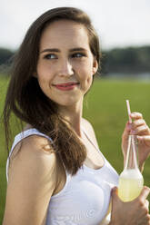 Smiling woman with lemonade juice bottle in nature - MIKF00086