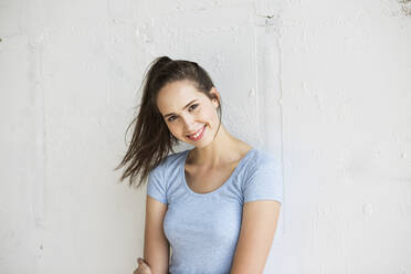 Happy woman with ponytail standing in front of wall - MIKF00089
