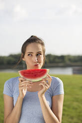 Frau mit Wassermelonenscheibe macht Gesicht im Park - MIKF00091