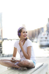 Nachdenkliche Frau mit Kopfhörern auf einer Bank sitzend - MIKF00097