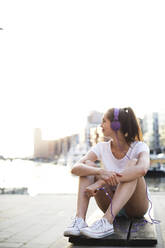 Young woman with headphones sitting on bench at promenade - MIKF00099