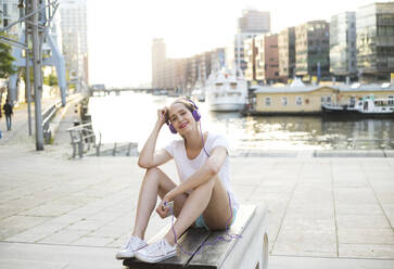 Smiling woman listening music through headphones at promenade - MIKF00100