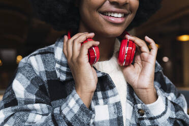 Young woman holding headphones in coffee shop - PNAF03332