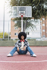 Young woman in casual clothing sitting on sports court - PNAF03340