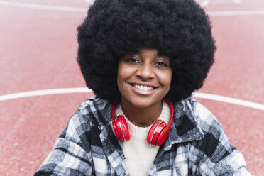 Junge Afro-Frau mit Kopfhörern lächelnd auf dem Sportplatz - PNAF03344