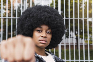 Confident woman showing fist in front of fence - PNAF03348