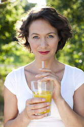 Frau im Park mit einem Glas frischen Orangensaft - MIKF00104