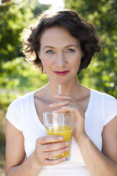 Woman in park with glass of fresh orange juice - MIKF00104