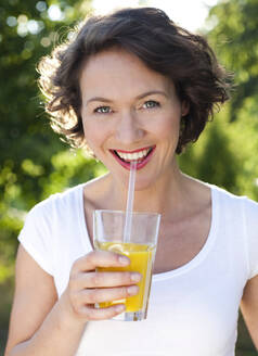 Glückliche Frau trinkt Orangensaft an einem sonnigen Tag - MIKF00106