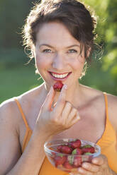 Smiling woman having strawberries on sunny day - MIKF00107