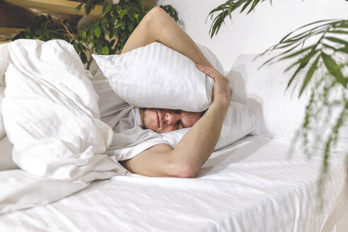 Man sleeping with pillow on head in bedroom at home - OMIF00688