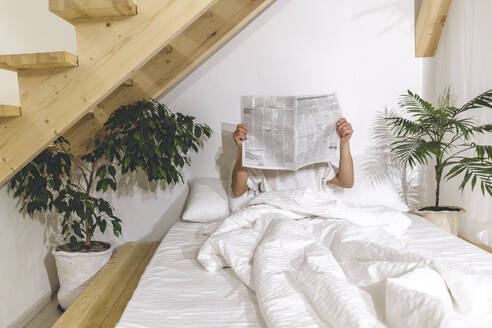 Mann liest Zeitung auf dem Bett sitzend zu Hause - OMIF00691