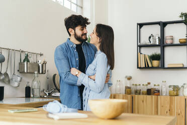 Smiling man embracing girlfriend standing in kitchen at home - GIOF14877