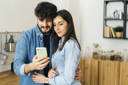 Junges Paar nimmt Selfie durch Handy in der Küche zu Hause - GIOF14887