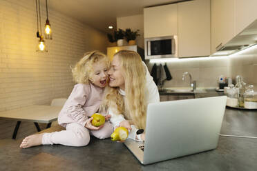 Woman with laptop and pears by daughter in kitchen - SIF00048