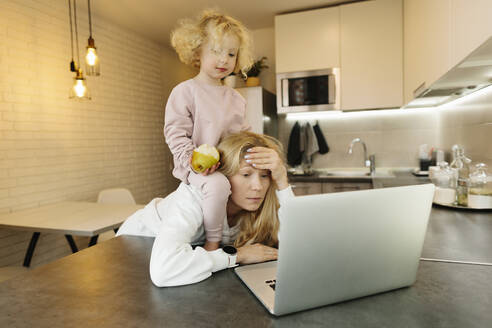 Müde Frau mit Tochter schaut auf Laptop in der Küche zu Hause - SIF00050