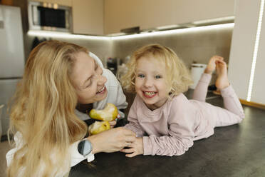Fröhliche Mutter und Tochter essen Birnen in der Küche zu Hause - SIF00051