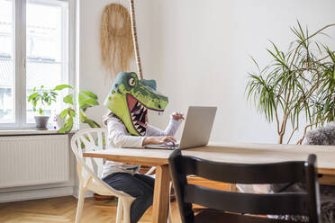 Girl with dinosaur mask using laptop at home - VGPF00063