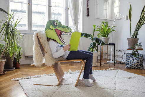 Mädchen mit Dinosauriermaske liest zu Hause ein Buch - VGPF00064