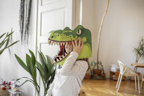 Mädchen mit Dinosaurier-Maske spricht zu Hause auf dem Smartphone - VGPF00070