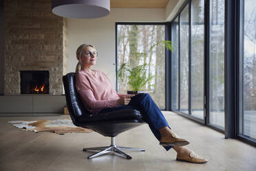 Thoughtful woman sitting with tablet PC on chair in living room - RBF08541