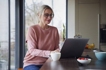 Blonde Frau benutzt Laptop in der Küche zu Hause - RBF08551