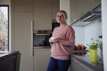 Blond woman holding coffee cup standing in kitchen - RBF08556