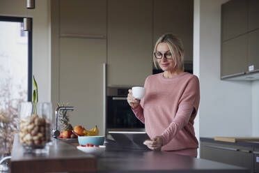 Blonde Frau mit Kaffeetasse und Tablet-PC in der Küche - RBF08557