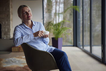 Blond woman with coffee cup sitting on chair at home - RBF08563