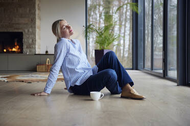 Blond woman with eyes closed siting on floor at home - RBF08567