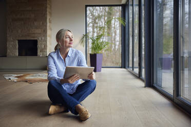 Woman holding tablet PC sitting cross-legged on floor at home - RBF08571