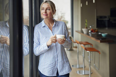 Blond woman holding coffee cup looking through window - RBF08577