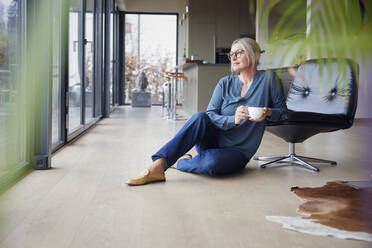 Blonde Frau mit Kaffeetasse sitzt auf einem Stuhl zu Hause - RBF08590