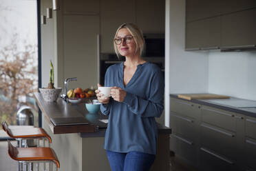 Frau hält Kaffeetasse stehend in Küche zu Hause - RBF08599