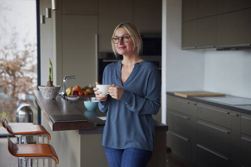 Frau hält Kaffeetasse stehend in Küche zu Hause - RBF08599