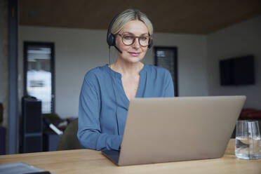 Lächelnde Frau mit Brille, die zu Hause einen Laptop benutzt - RBF08602