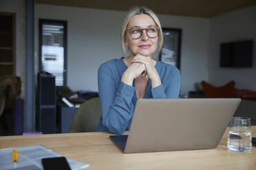 Blond woman wearing eyeglasses sitting with hand on chin at table - RBF08604