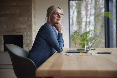 Blonde Frau sitzt mit Hand am Kinn am Tisch - RBF08606