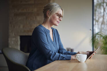 Blond woman using tablet PC sitting at table - RBF08607