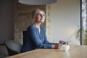 Frau mit Brille sitzt mit Tablet-PC am Tisch - RBF08608