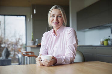 Smiling blond woman holding coffee cup sitting at table - RBF08611