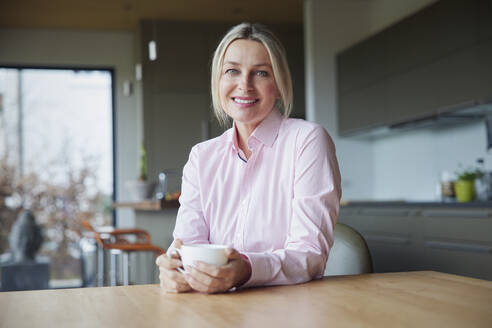 Lächelnde blonde Frau mit Kaffeetasse am Tisch sitzend - RBF08611