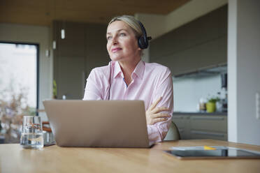 Frau mit Kopfhörern sitzt mit Laptop am Tisch - RBF08616