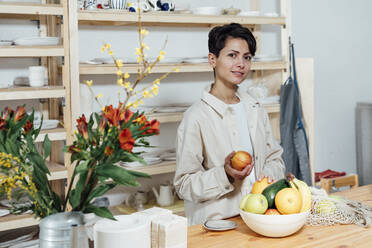 Unternehmerin mit Schale mit Früchten am Tisch stehend - VPIF05540