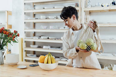 Entrepreneur holding mesh bag of fresh fruit by table - VPIF05545
