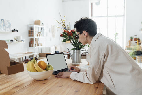 Entrepreneur working on laptop leaning on table in store - VPIF05556