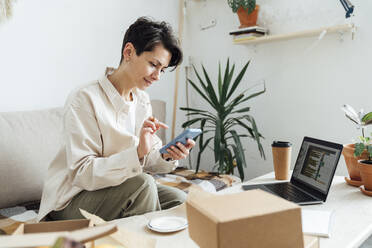 Entrepreneur using smart phone with boxes at store - VPIF05560