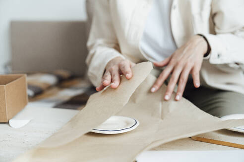 Handwerkerin beim Verpacken von Keramiktellern in Packpapier für den Versand - VPIF05563