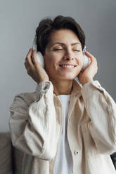 Lächelnde Frau mit geschlossenen Augen, die mit Kopfhörern Musik hört - VPIF05588